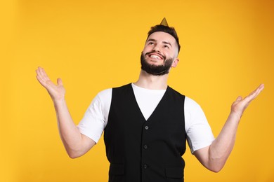 Photo of Happy Birthday. Handsome man with party hat on orange background