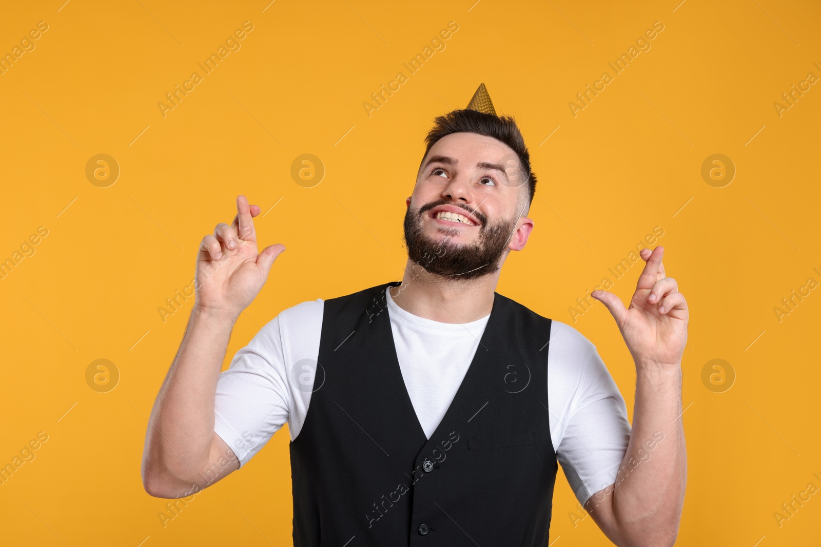 Happy Birthday. Handsome man with party hat crossing fingers while making wish on orange background Photo of Happy Birthday. Handsome man with party hat crossing fingers while making wish on orange background