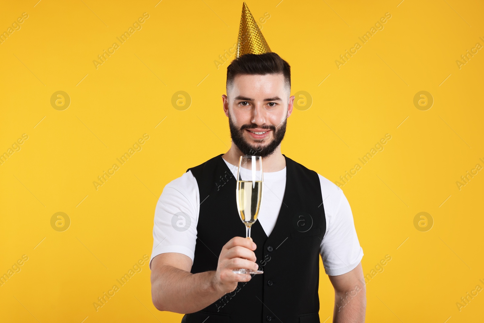 Happy Birthday. Handsome man with party hat and glass of champagne on orange background Photo of Happy Birthday. Handsome man with party hat and glass of champagne on orange background