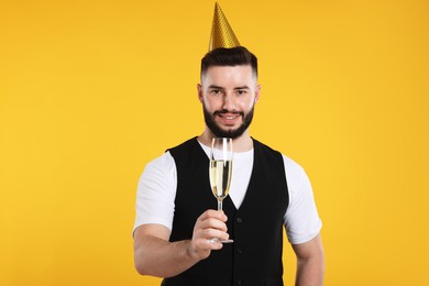 Photo of Happy Birthday. Handsome man with party hat and glass of champagne on orange background