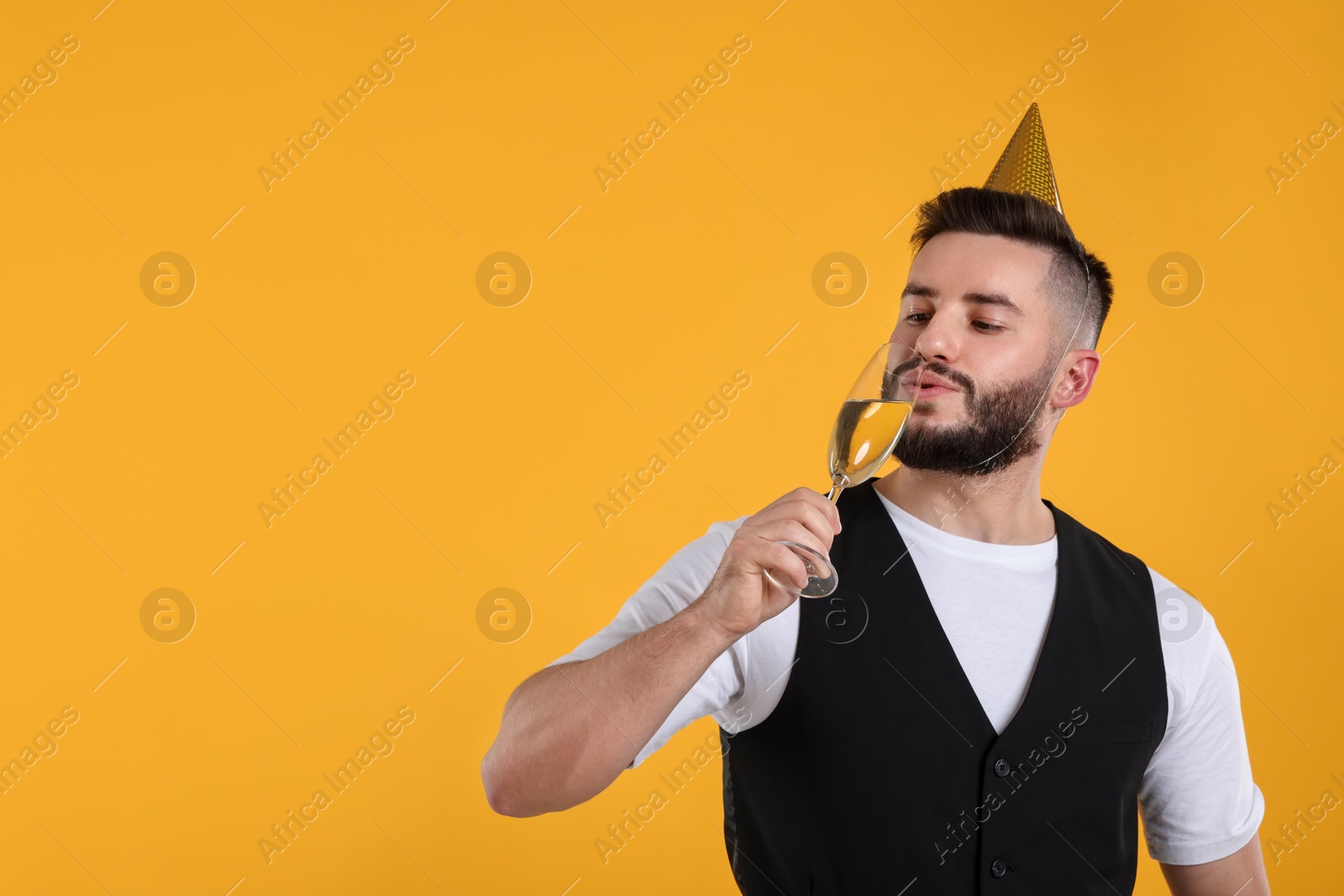Happy Birthday. Handsome man with party hat and glass of champagne on orange background, space for text Photo of Happy Birthday. Handsome man with party hat and glass of champagne on orange background, space for text