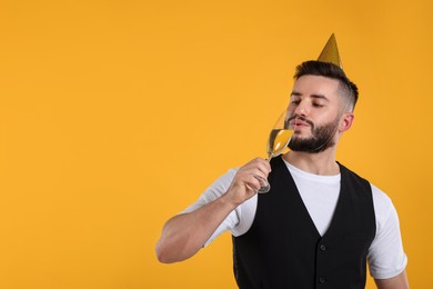 Photo of Happy Birthday. Handsome man with party hat and glass of champagne on orange background, space for text