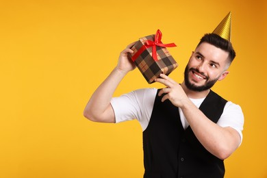 Photo of Happy Birthday. Handsome man with party hat and gift box on orange background, space for text