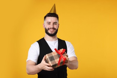 Photo of Happy Birthday. Handsome man with party hat and gift box on orange background, space for text