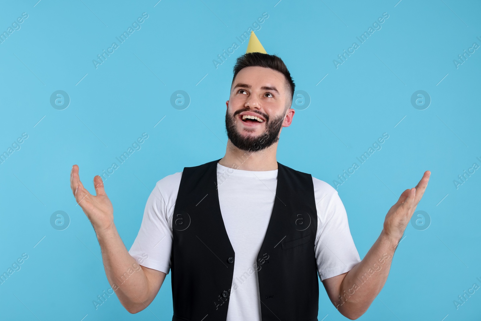 Happy Birthday. Handsome man with party hat on light blue background Photo of Happy Birthday. Handsome man with party hat on light blue background