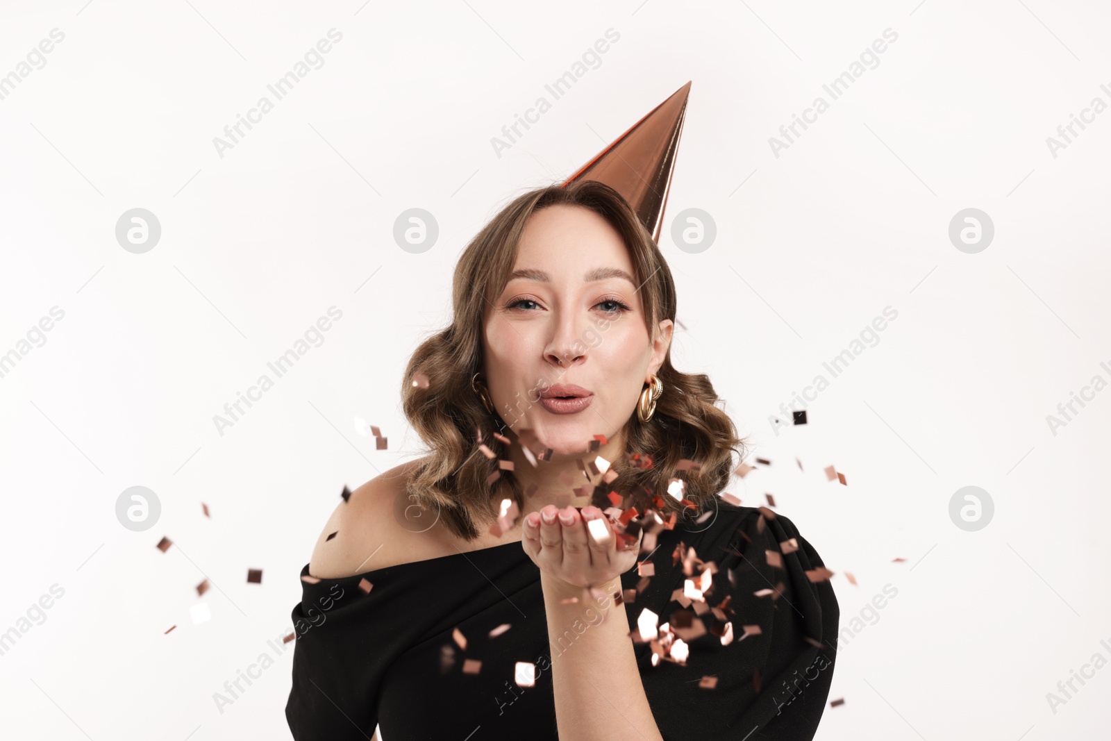Birthday celebration. Woman with party cone blowing confetti on white background Photo of Birthday celebration. Woman with party cone blowing confetti on white background