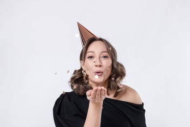 Photo of Birthday celebration. Woman with party cone blowing confetti on white background