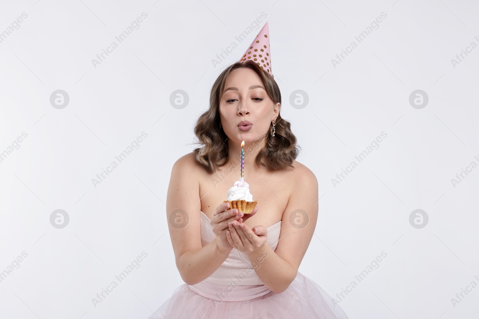 Birthday celebration. Woman blowing candle on cupcake against white background Photo of Birthday celebration. Woman blowing candle on cupcake against white background