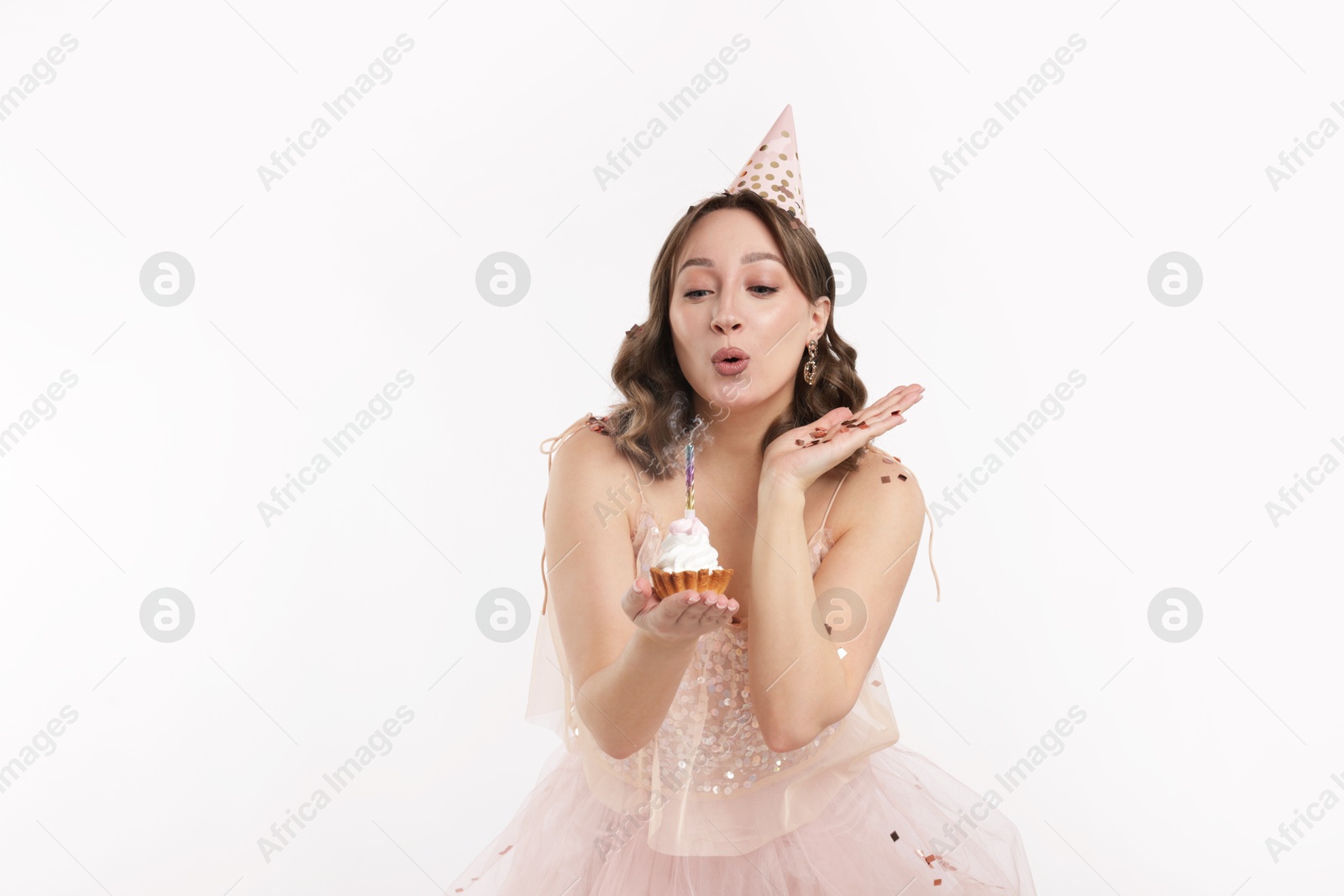Birthday celebration. Woman blowing candle on cupcake and confetti against white background Photo of Birthday celebration. Woman blowing candle on cupcake and confetti against white background