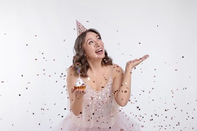 Photo of Birthday celebration. Woman with cupcake and confetti on white background