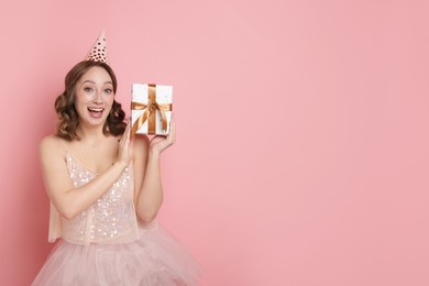 Photo of Birthday celebration. Woman with gift on pink background. Space for text