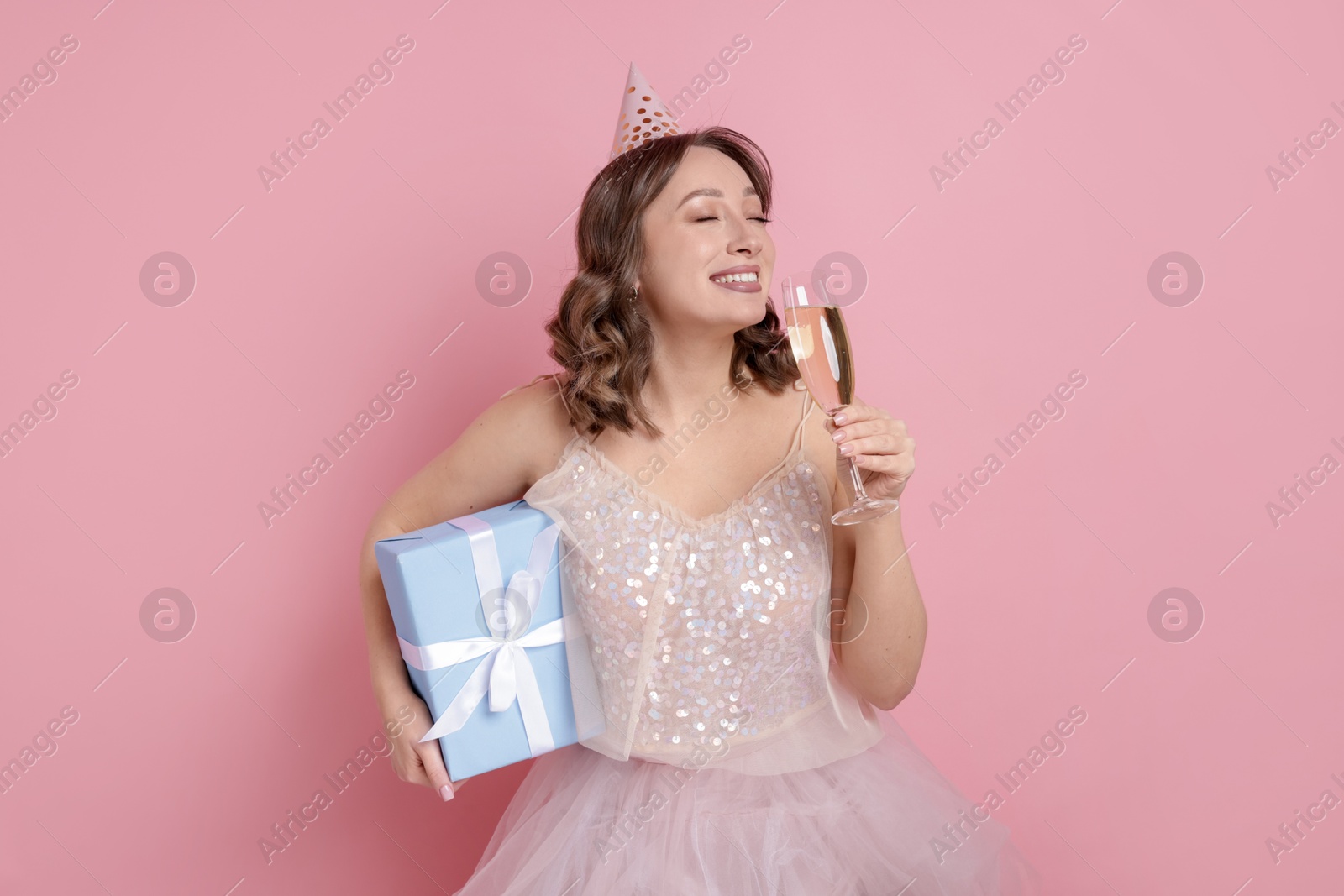 Birthday celebration. Woman with glass of sparkling wine and gift on pink background Photo of Birthday celebration. Woman with glass of sparkling wine and gift on pink background