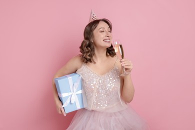 Photo of Birthday celebration. Woman with glass of sparkling wine and gift on pink background