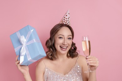 Photo of Birthday celebration. Woman with glass of sparkling wine and gift on pink background