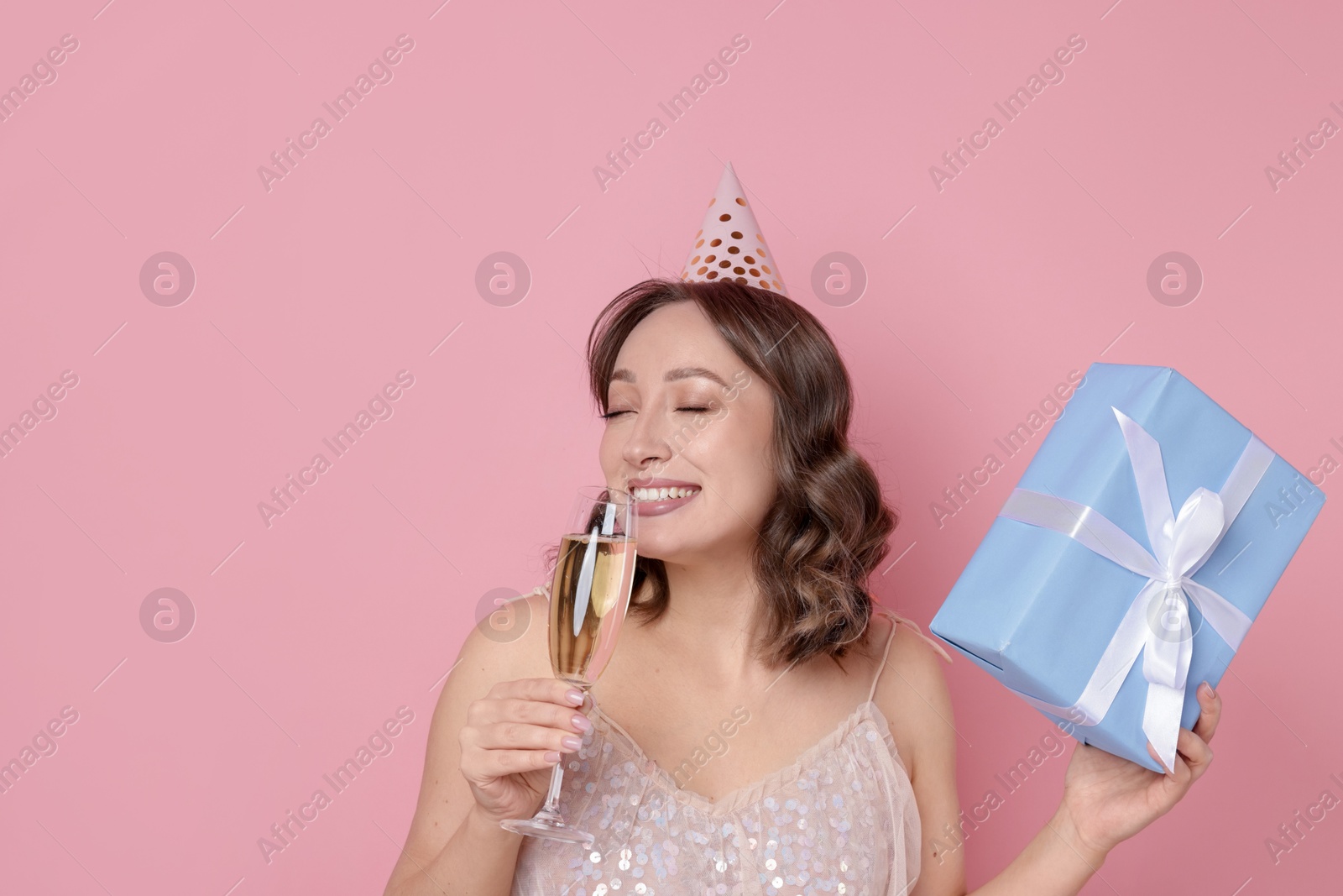 Birthday celebration. Woman with glass of sparkling wine and gift on pink background Photo of Birthday celebration. Woman with glass of sparkling wine and gift on pink background