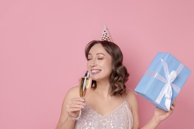 Photo of Birthday celebration. Woman with glass of sparkling wine and gift on pink background
