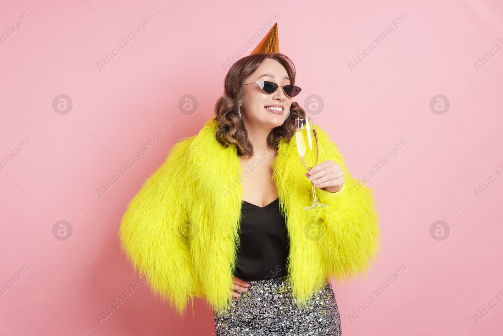 Birthday celebration. Woman with glass of sparkling wine on pink background Photo of Birthday celebration. Woman with glass of sparkling wine on pink background