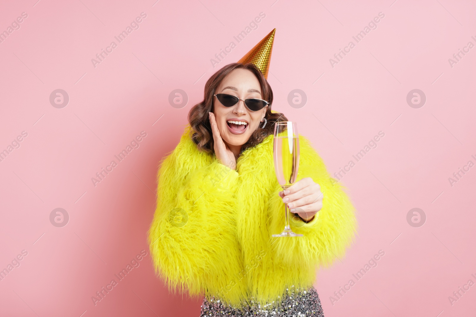 Birthday celebration. Woman with glass of sparkling wine on pink background Photo of Birthday celebration. Woman with glass of sparkling wine on pink background