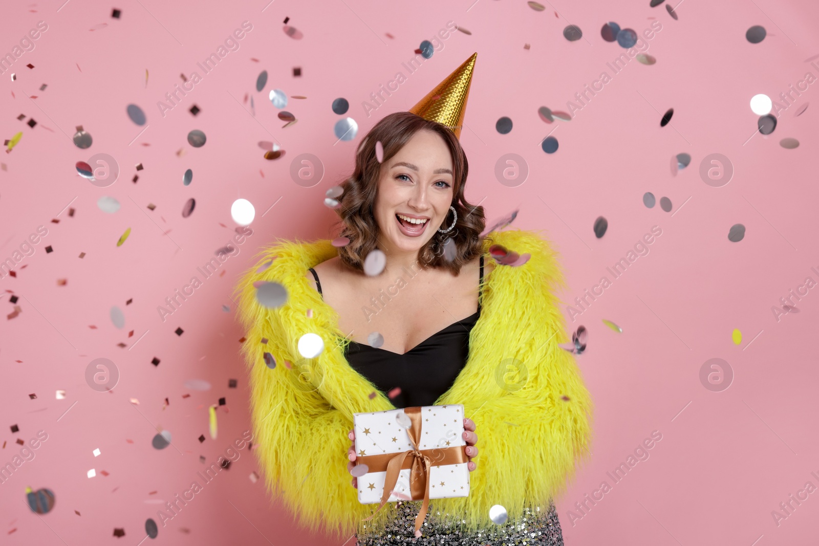 Birthday celebration. Woman with gift and confetti on pink background Photo of Birthday celebration. Woman with gift and confetti on pink background