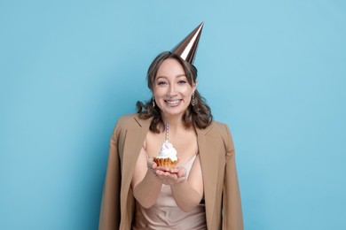 Photo of Birthday celebration. Woman with cupcake on light blue background