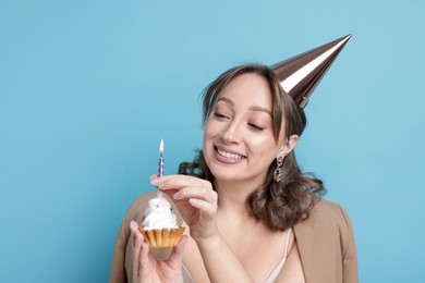 Photo of Birthday celebration. Woman with cupcake on light blue background. Space for text