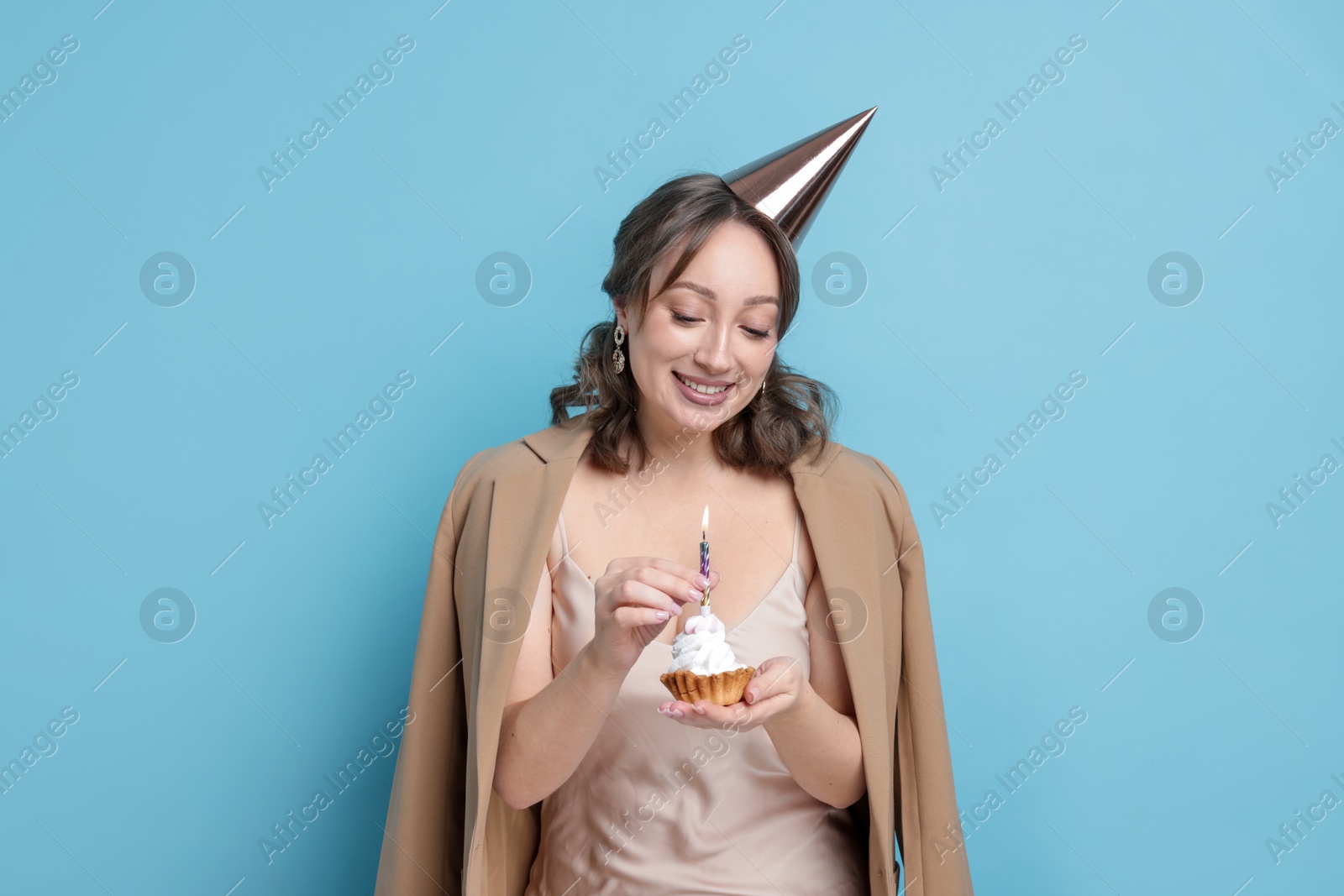 Birthday celebration. Woman with cupcake on light blue background Photo of Birthday celebration. Woman with cupcake on light blue background
