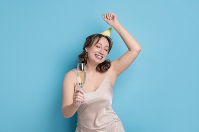 Photo of Birthday celebration. Woman with glass of sparkling wine on light blue background