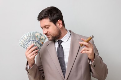 Photo of Greedy banker with dollar banknotes smoking cigar on grey background
