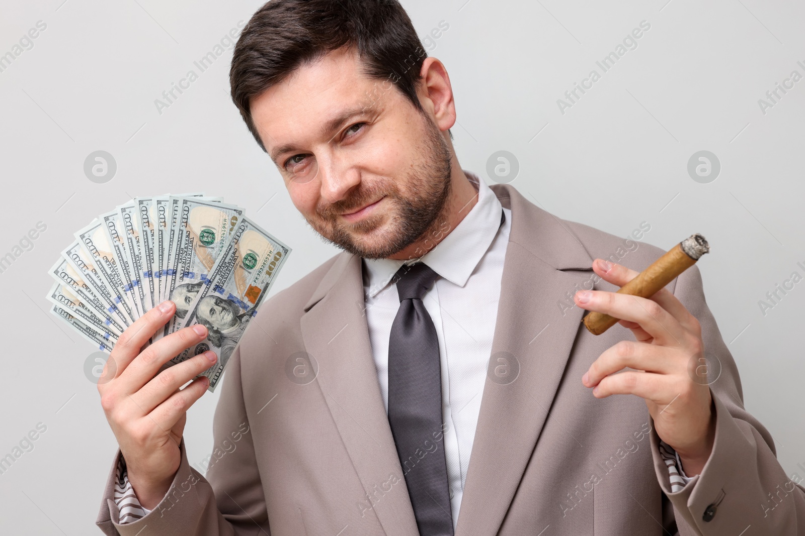 Greedy banker with dollar banknotes smoking cigar on grey background Photo of Greedy banker with dollar banknotes smoking cigar on grey background
