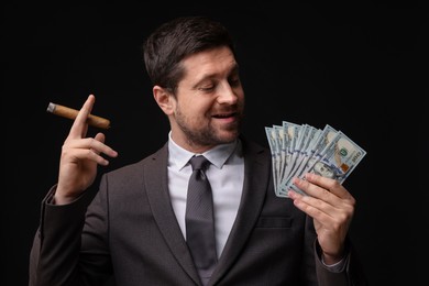 Photo of Greedy banker with dollar banknotes smoking cigar on black background