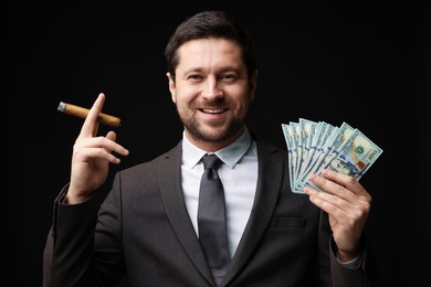 Photo of Happy greedy banker with dollar banknotes smoking cigar on black background