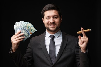 Photo of Happy greedy banker with dollar banknotes smoking cigar on black background