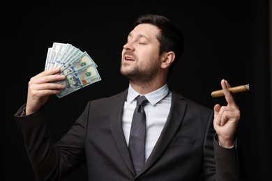 Photo of Greedy banker with dollar banknotes smoking cigar on black background