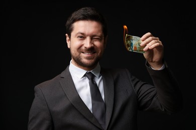 Photo of Happy greedy banker with burning dollar banknote on black background