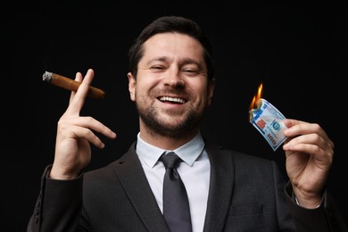 Photo of Happy greedy banker with burning dollar banknote smoking cigar on black background