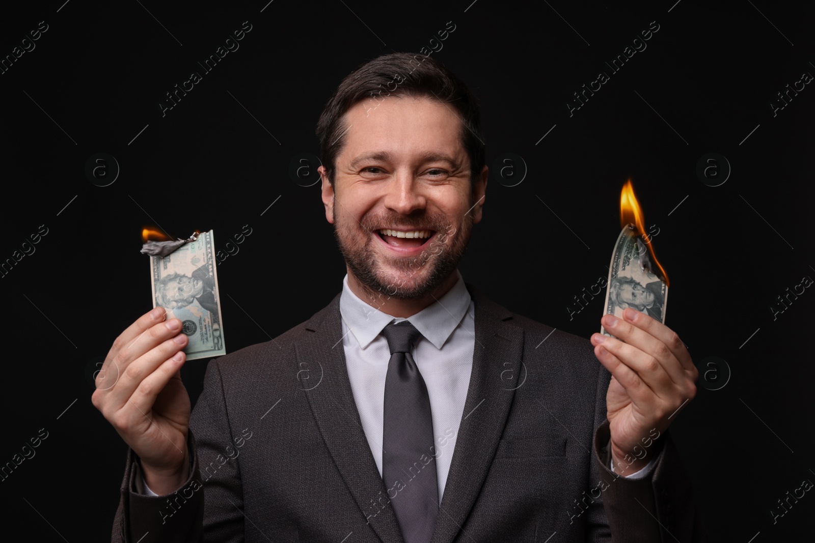 Happy greedy banker with burning dollar banknotes on black background Photo of Happy greedy banker with burning dollar banknotes on black background