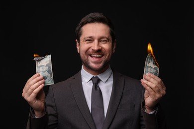 Photo of Happy greedy banker with burning dollar banknotes on black background