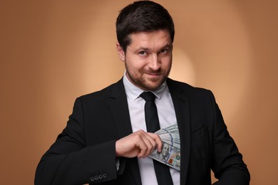 Photo of Greedy banker hiding money into inner pocket of suit on golden background