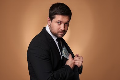 Photo of Greedy banker hiding money into inner pocket of suit on golden background