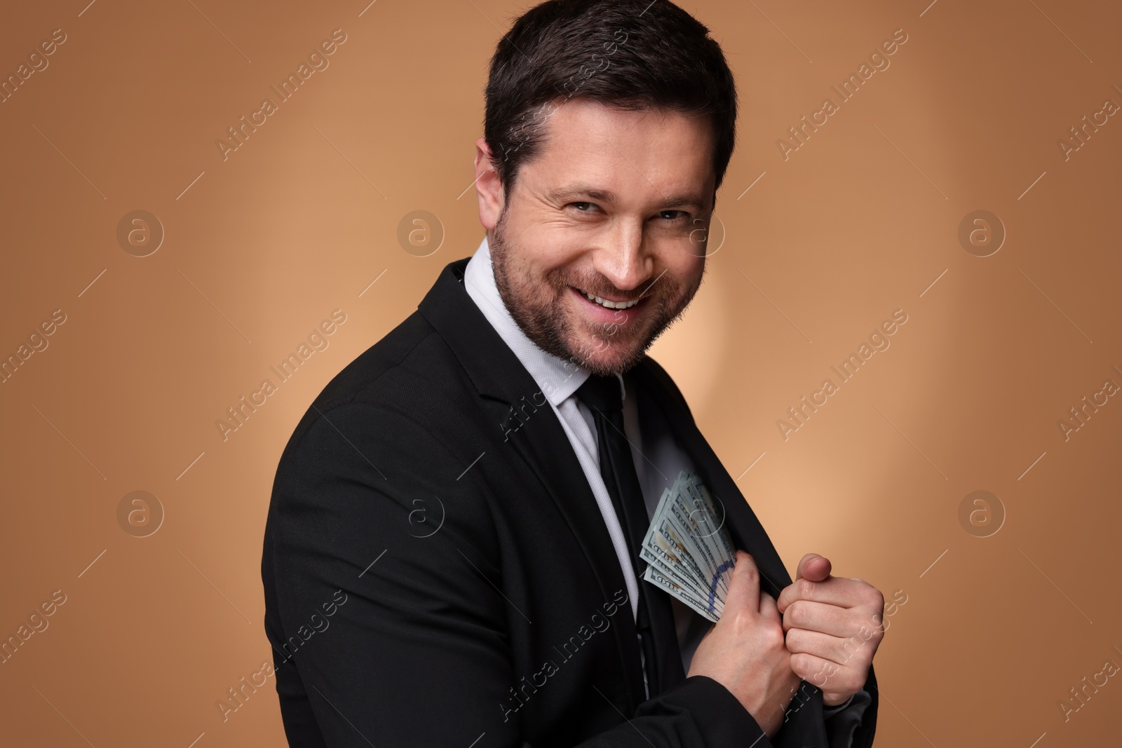 Happy greedy banker hiding money into inner pocket of suit on golden background Photo of Happy greedy banker hiding money into inner pocket of suit on golden background
