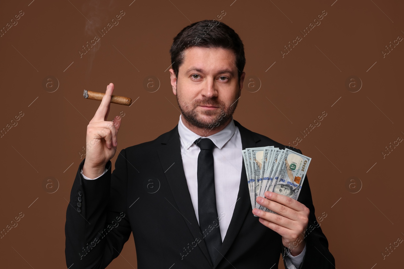 Greedy banker with dollar banknotes smoking cigar on brown background Photo of Greedy banker with dollar banknotes smoking cigar on brown background
