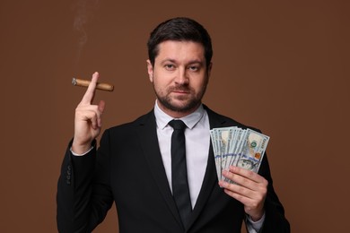 Photo of Greedy banker with dollar banknotes smoking cigar on brown background