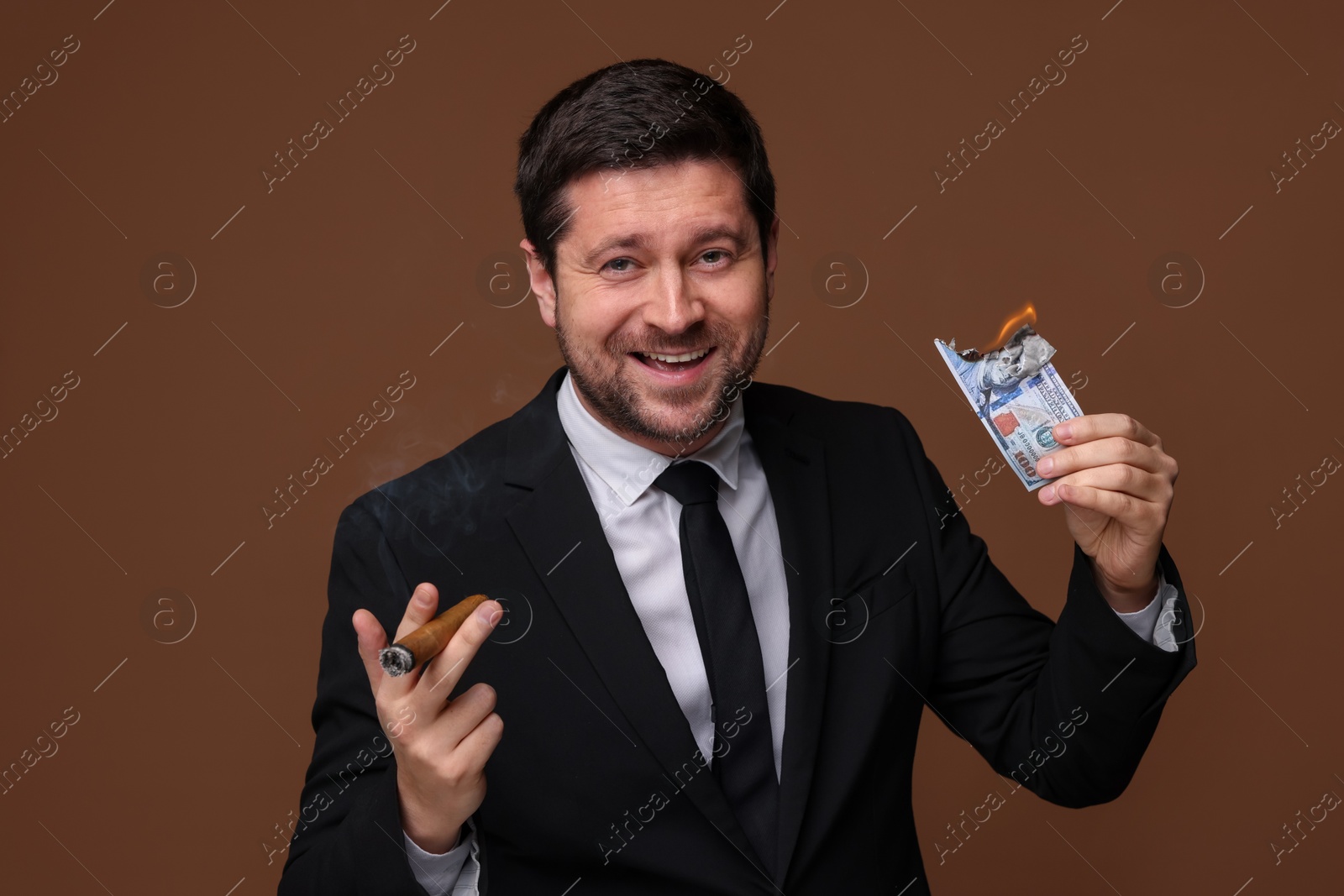 Happy greedy banker with burning dollar banknote smoking cigar on brown background Photo of Happy greedy banker with burning dollar banknote smoking cigar on brown background