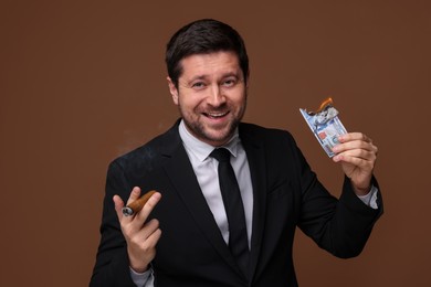 Photo of Happy greedy banker with burning dollar banknote smoking cigar on brown background