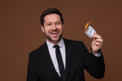 Photo of Happy greedy banker with burning dollar banknote on brown background
