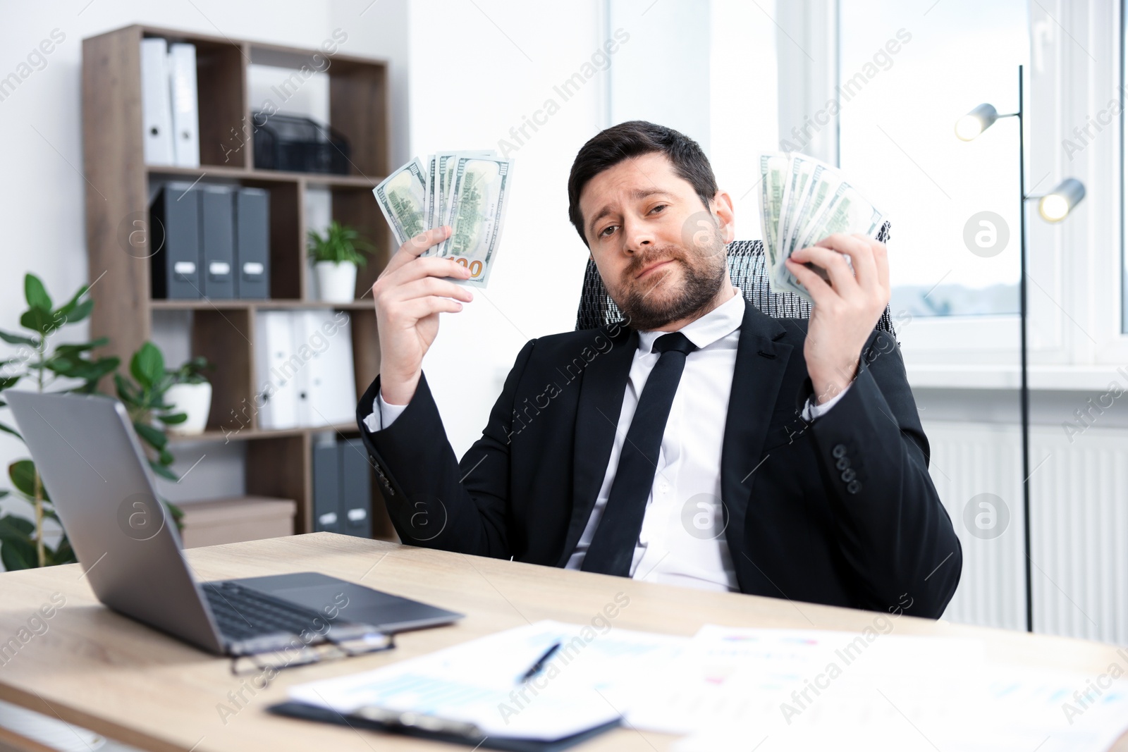 Greedy banker with dollar banknotes at table in office Photo of Greedy banker with dollar banknotes at table in office