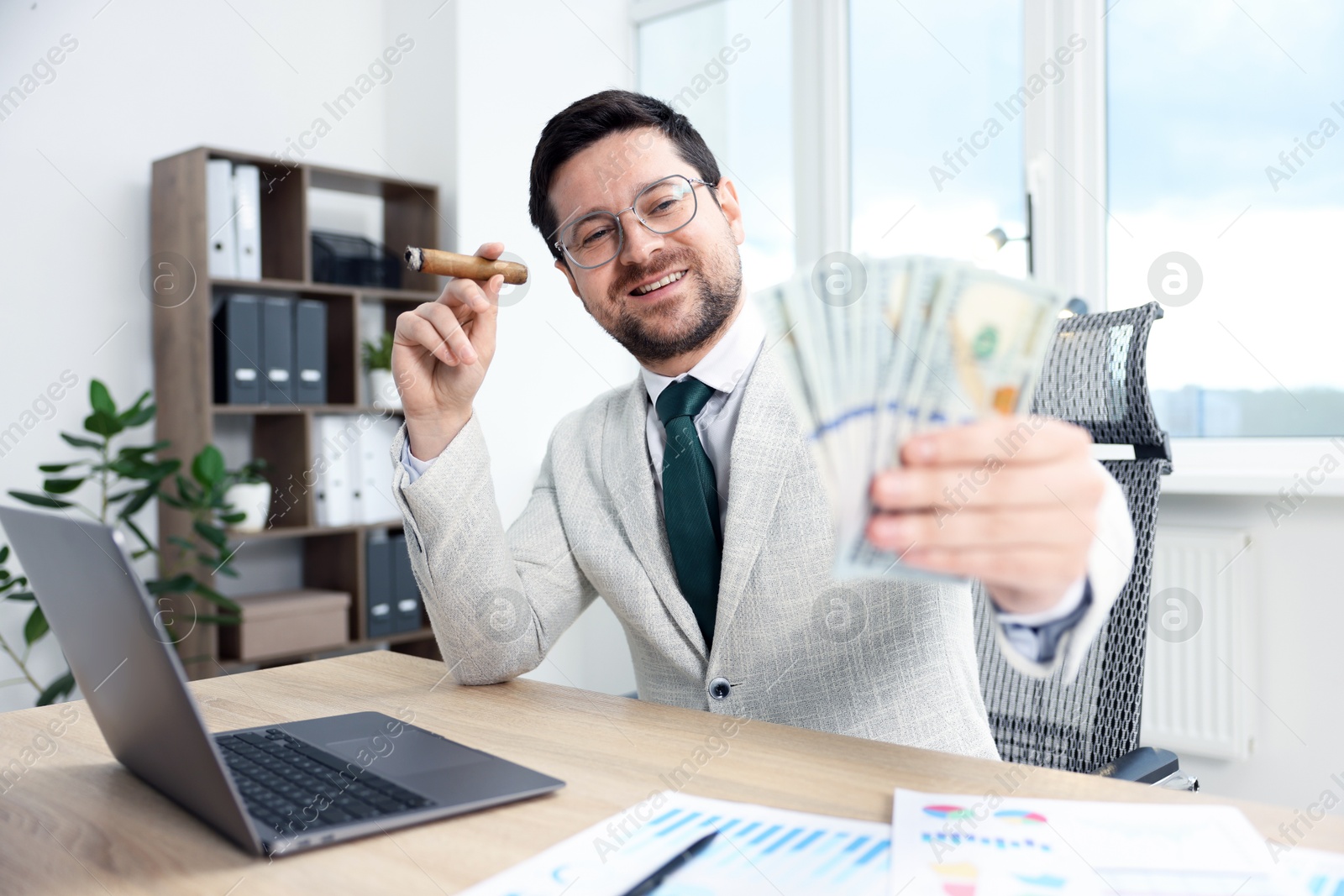 Happy greedy banker with dollar banknotes and cigar at table in office, selective focus Photo of Happy greedy banker with dollar banknotes and cigar at table in office, selective focus