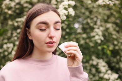 Photo of Woman with paper tissue suffering from seasonal pollen allergy near blossoming shrub on spring day, space for text
