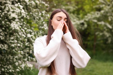 Photo of Woman suffering from seasonal pollen allergy near blossoming shrub on spring day