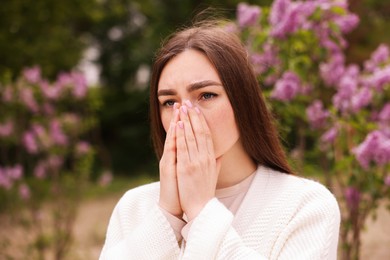 Photo of Woman suffering from seasonal pollen allergy near blossoming shrub on spring day